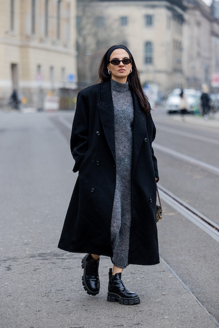 Modella con abito grigio e borsa, stivali e cappotto neri