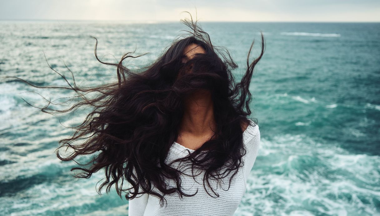 ragazza mora capelli scuri al vento con sfondo mare turchese