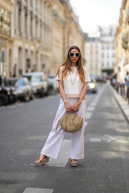 ragazza con completo bianco, zeppe in rafia e borsa di paglia