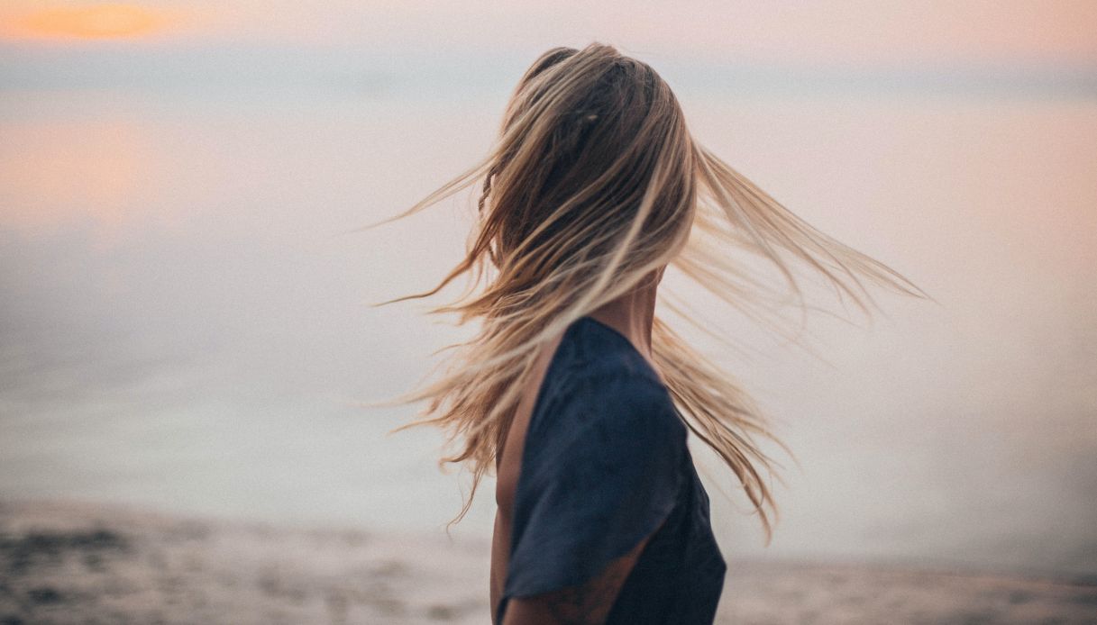 ragazza bionda di spalle con vista mare e capelli al vento