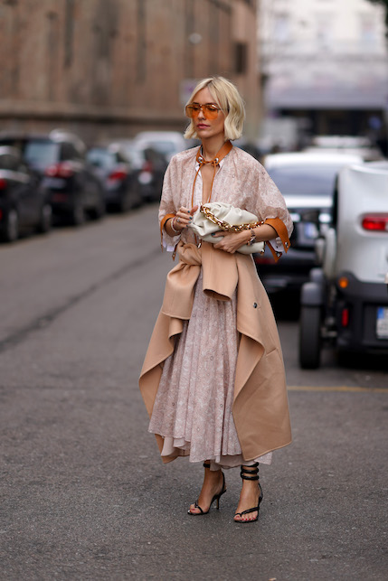 Modella con abito lungo in seta chiaro, cappotto beige e occhiali