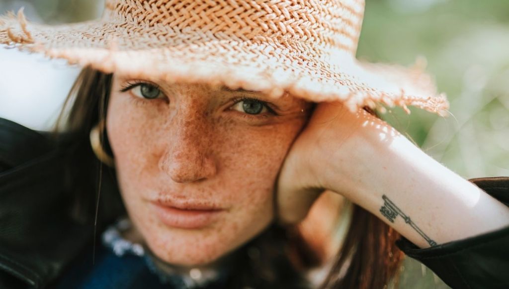 primo piano ragazza mano appoggiata volto occhi chiari lentiggini cappello