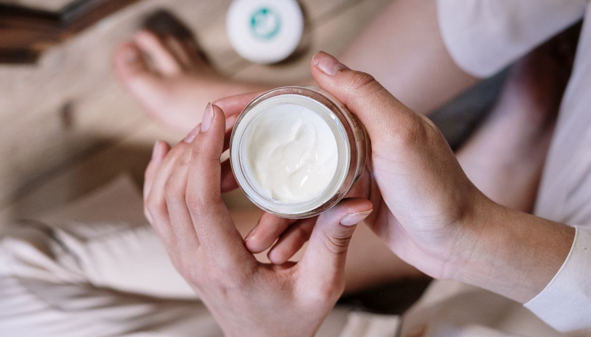 mani di donna con barattolo di crema e gambe incrociate
