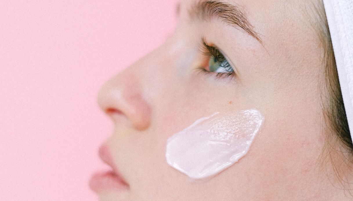 viso femminile con occhi azzurri e crema sullo zigomo su sfondo rosa