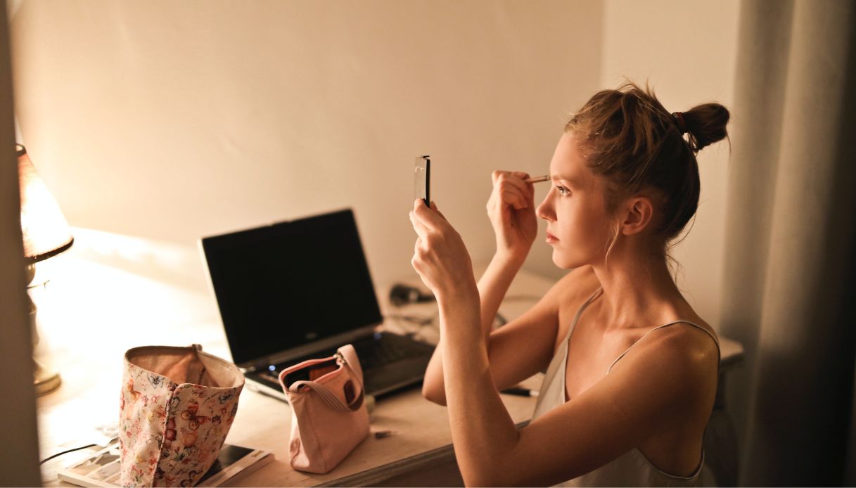 ragazza alla scrivània davanti al pc si trucca con uno specchietto
