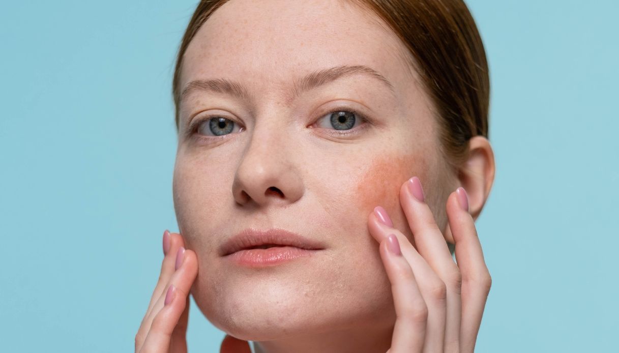 sfondo azzurro, donna con capelli raccolti, pelle chiara e occhi azzurri, applica blush sulle guance