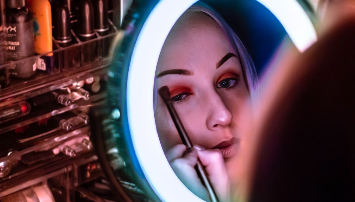 ragazza allo specchio si trucca nel riflesso con ombretto rosso