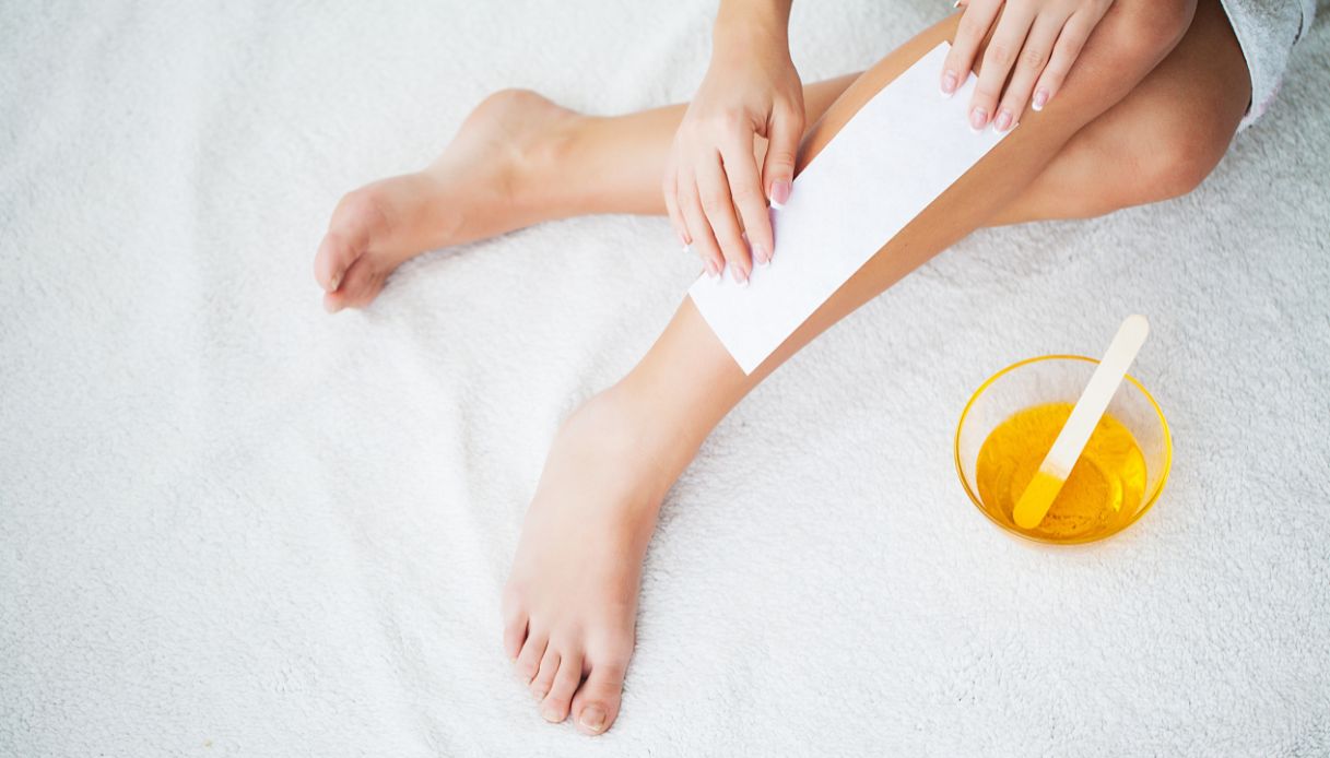 donna con gambe incrociate su lenzuolo bianco fa ceretta con strisce