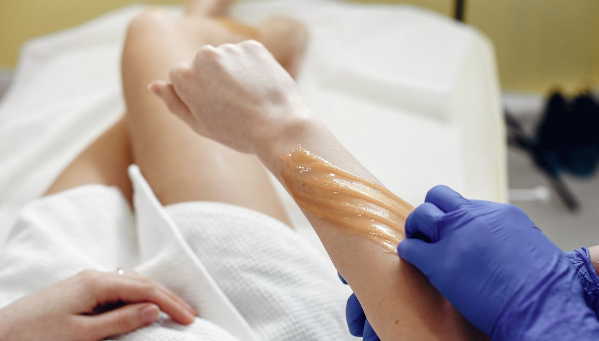 ceretta a freddo ralingata da mani con guanti blu su braccio di donna sdraiata con accappatoio bianco 