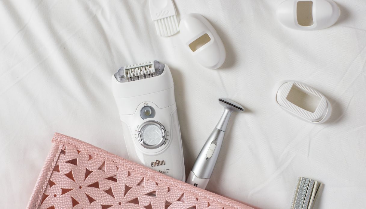 beauty case rosa da cui fuoriescono rasoi di vario tipo su sfondo bianco