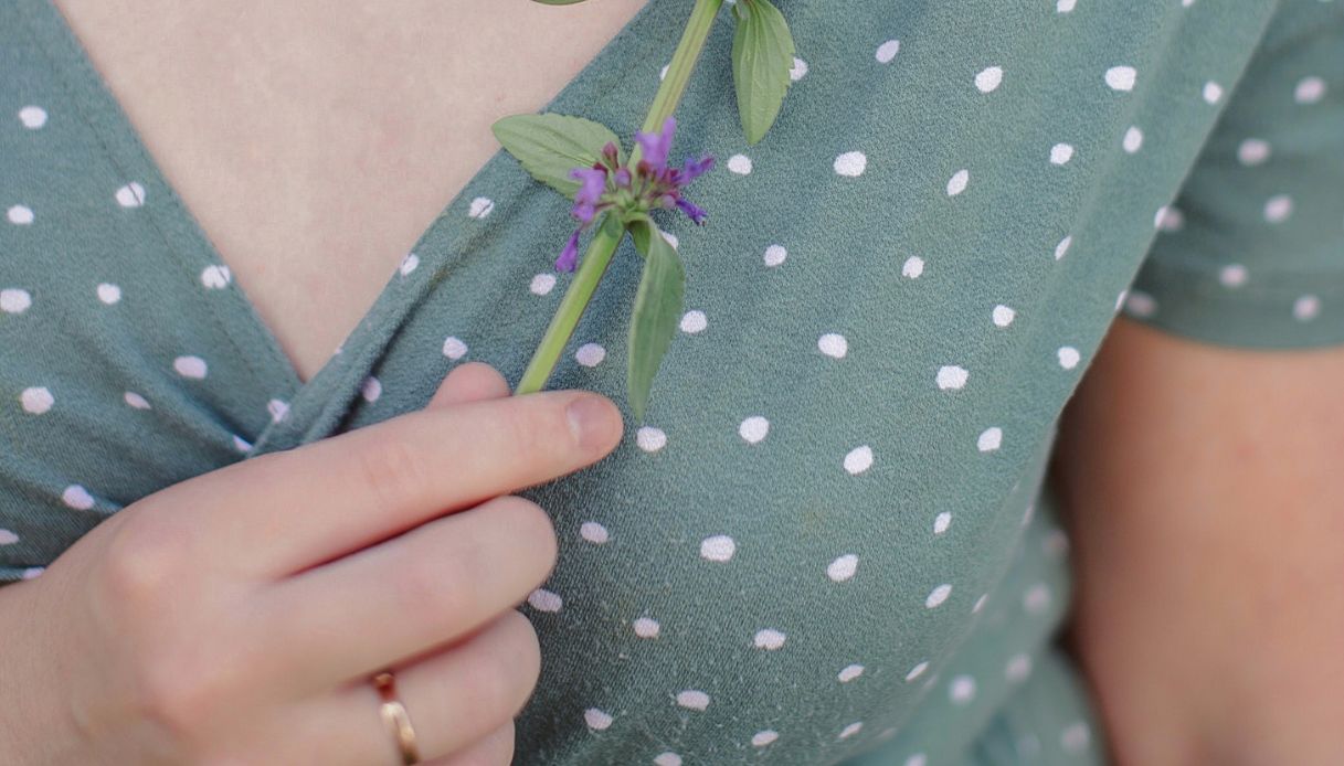 scollo a v di vestito verde salvia a pois bianchi e mano di donna con anello che porta fiori di lavanda al seno