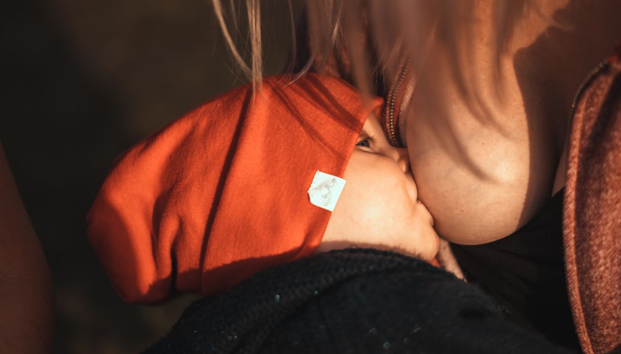 bambino neonato vestito di nero con cappellino arancione è attaccato al seno di una donna bionda
