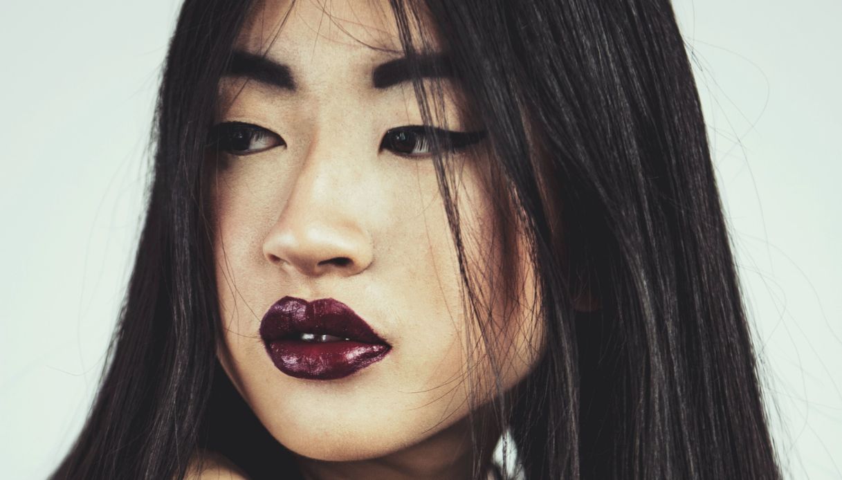 ragazza asiatica con capelli neri sugli occhi e labbra carnose con rossetto viola scuro lucido