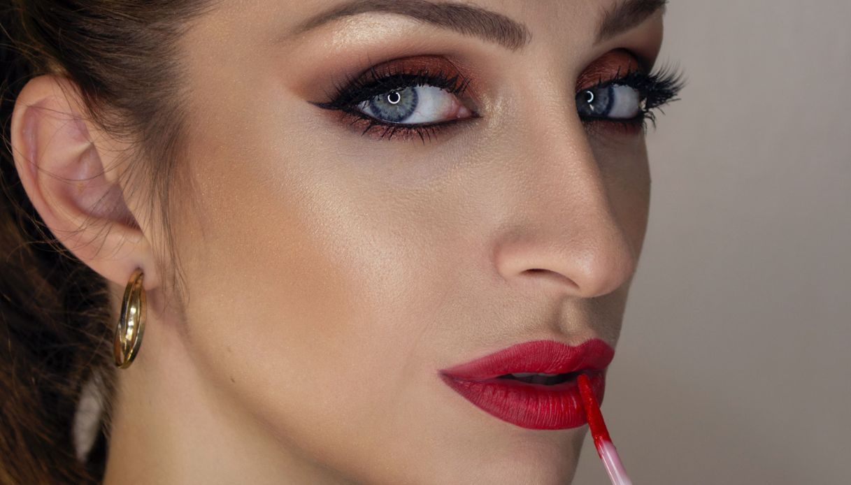 donna con occhi azzurri e trucco sugli occhi applica rossetto rosso con pennello