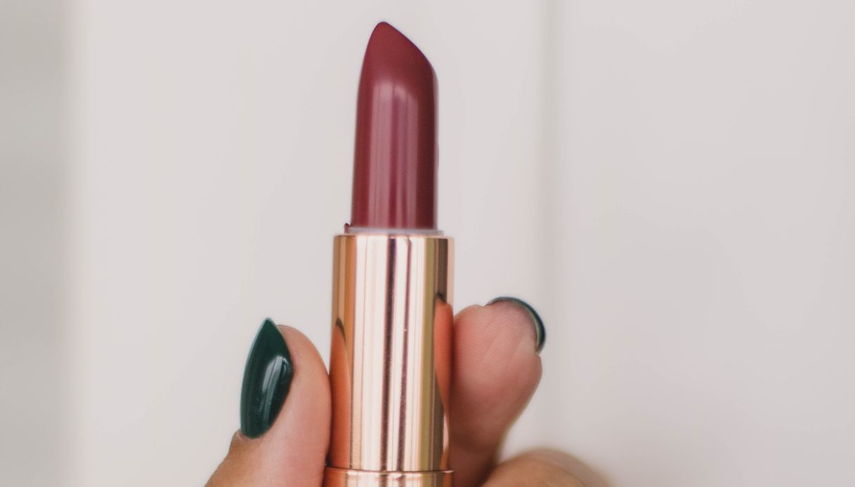 primo piano di rossetto rosso scuro con pack oro e mano con unghie verdi