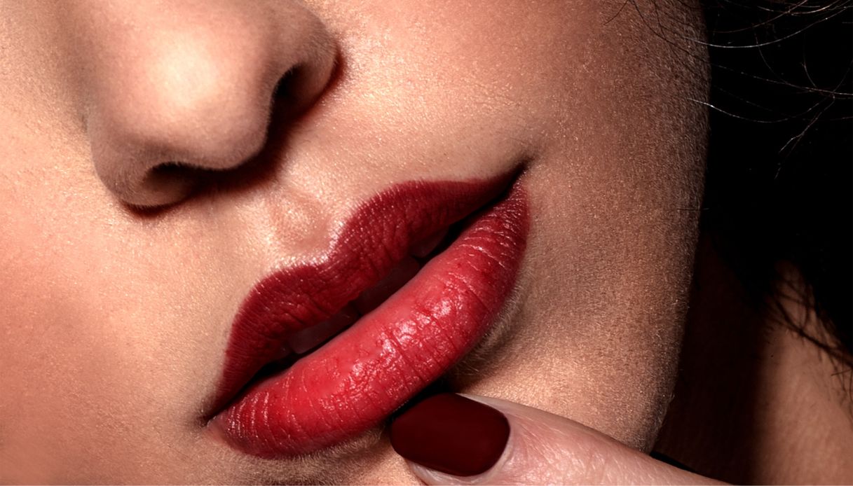 primo piano di labbra rosse e dito con unghia scura