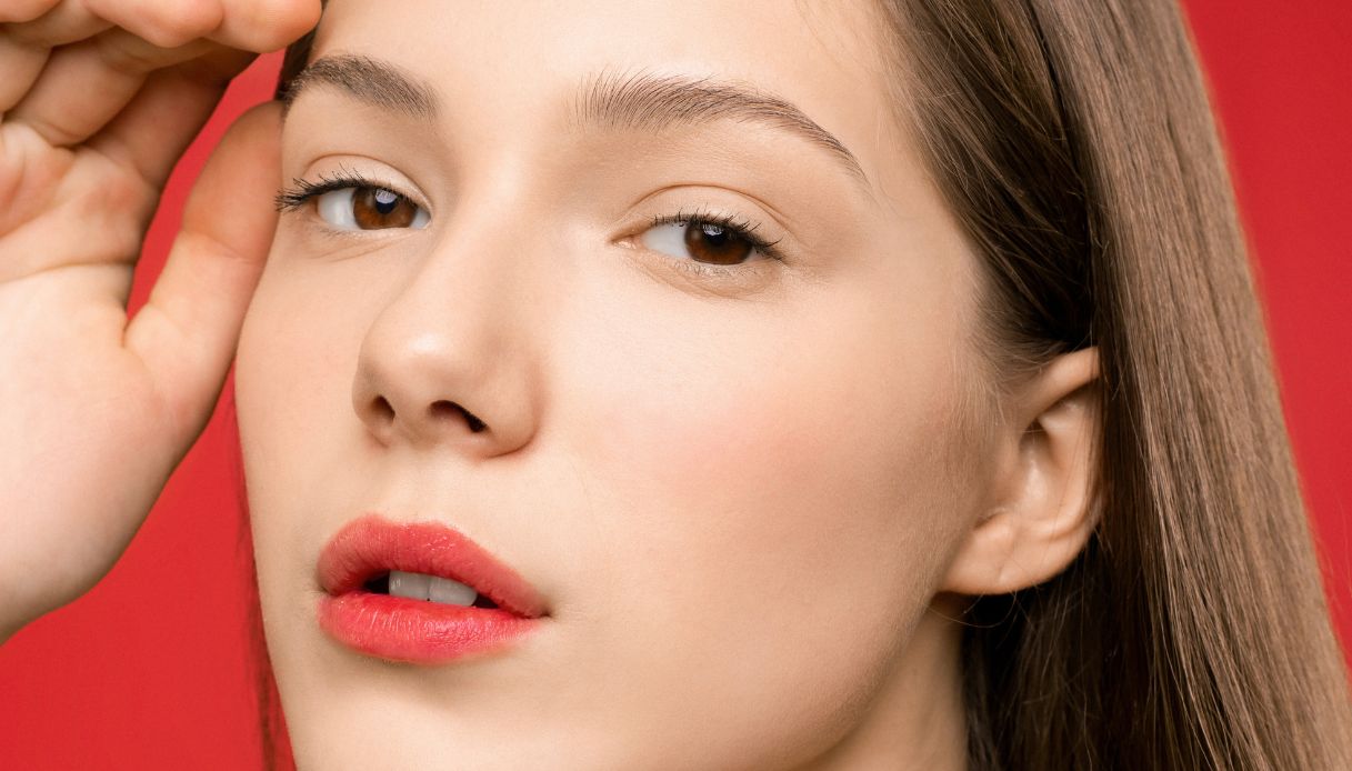 ragazza biondo cenere con rossetto rosso si tocca la testa su sfondo rosso