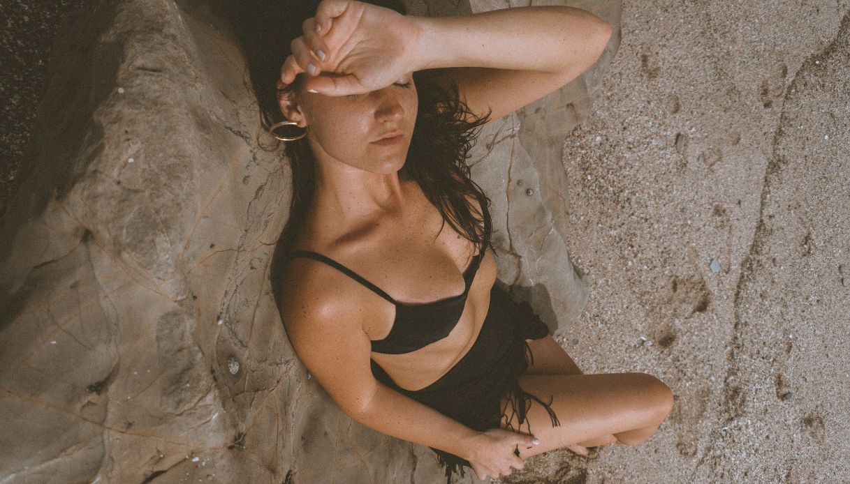 donna con costume nero sdraiata sulla spiaggia a prendere il sole si copre gli occhi con la mano