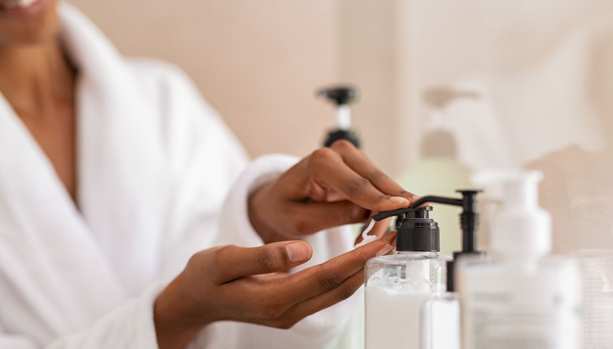 primo piano mani donna nera con accappatoio bianco che preleva crema bianca da tubetto