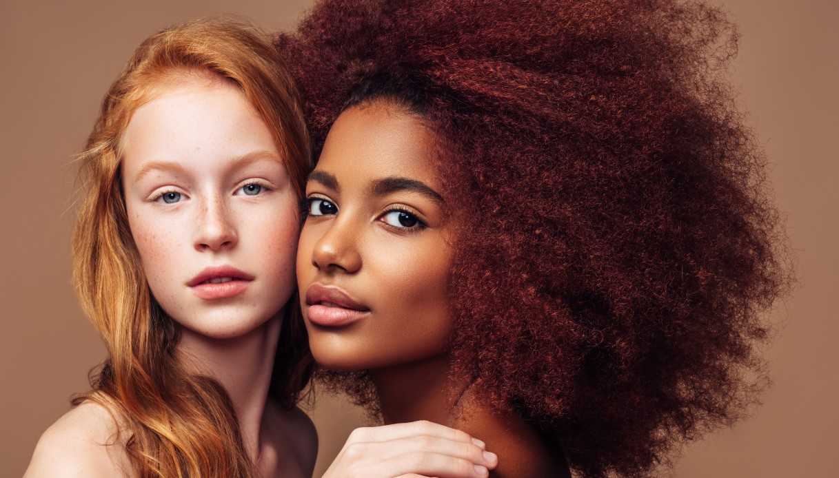 Una ragazza bianca rossa naturale con i capelli lunghi abbraccia una ragazza nera con i capelli ricci tinti di rosso scuro