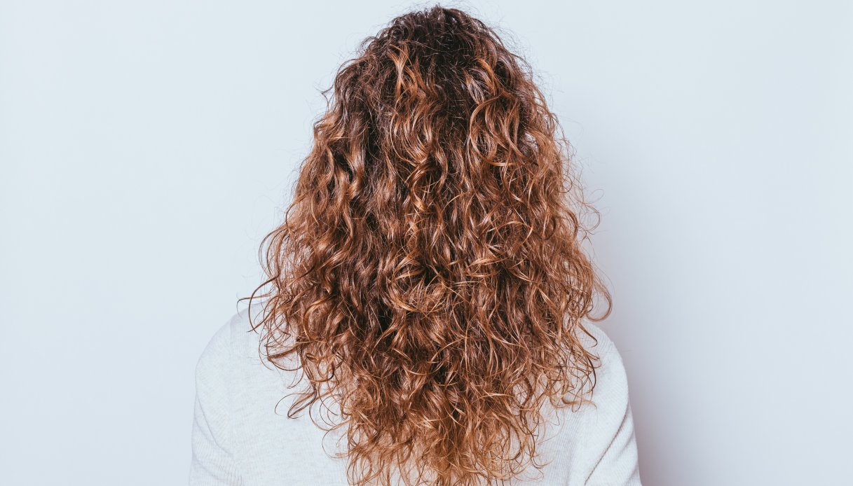 Donna di spalle con capelli lunghi e naturalmente ricci su sfondo bianco.