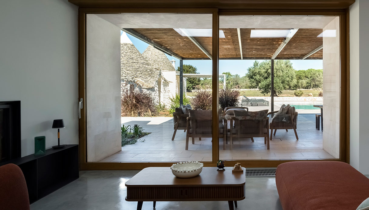 Il soggiorno si apre sulla veranda e la piscina, offrendo continuità visiva e un’immersione totale nella natura
