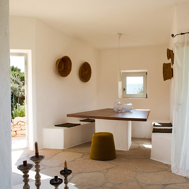 La zona pranzo con panche integrate e toni neutri interpreta il design mediterraneo in chiave minimale