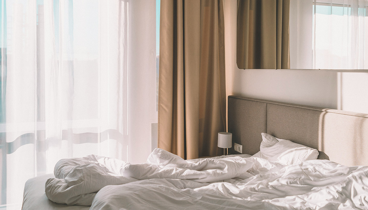 Camera da letto luminosa con tende beige e lenzuola bianche spiegazzate