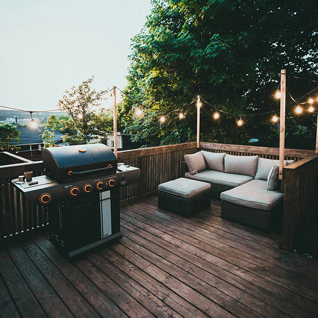 Ghirlande luminose e arredi in legno per un terrazzo caldo e accogliente, ideale per barbecue e relax